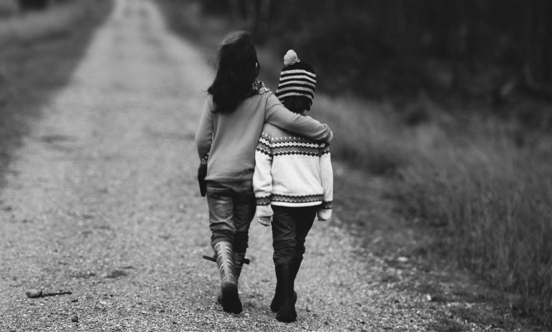 Deux enfants marchent côte à côte sur un chemin, l'un tenant l'autre par l'épaule.